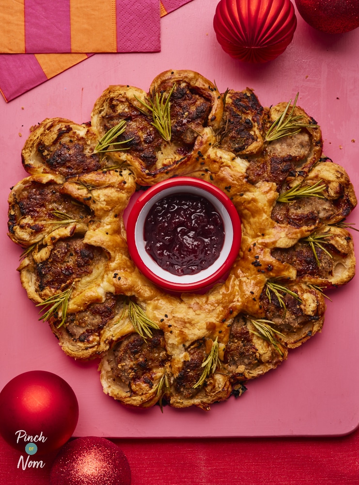 Pinch of Nom Sausage Roll Wreath, fully assembled and baked, with pot of cranberry sauce placed in the centre.