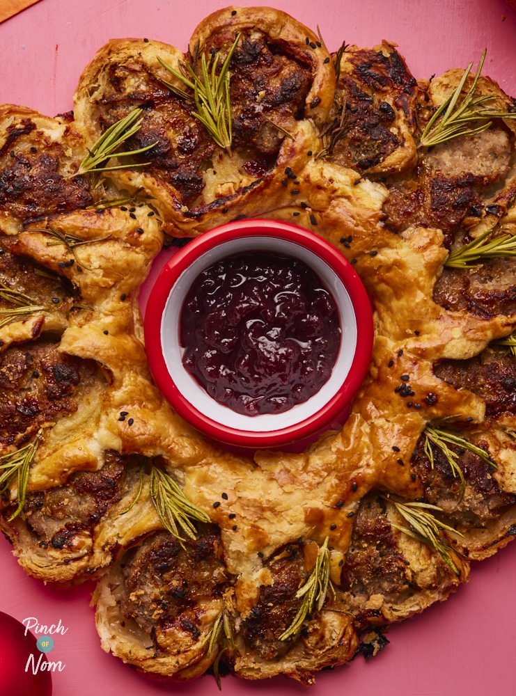 Pinch of Nom Sausage Roll Wreath, fully assembled and baked, with pot of cranberry sauce placed in the centre.